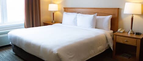 A neatly made bed with white linens, two bedside lamps, a wooden nightstand, and a window with curtains.