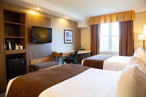 Habitación de hotel con dos camas, un escritorio, una silla, un televisor y una ventana con cortinas.