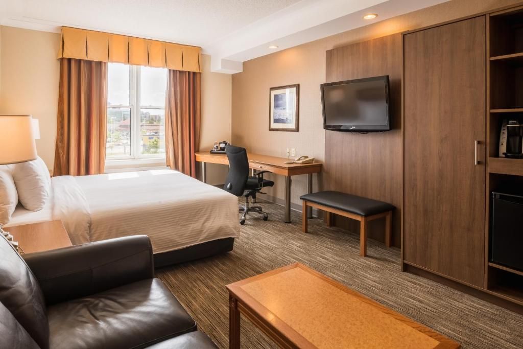 A hotel room with a bed, a desk, a television, a sofa, and a coffee machine.