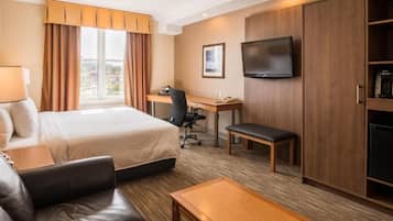 A hotel room with a bed, a desk, a television, a sofa, and a coffee machine.