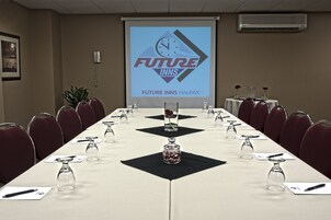 A conference room with a long table set for a meeting, a projector screen displaying "Future Inns Halifax", and a clock on the screen.
