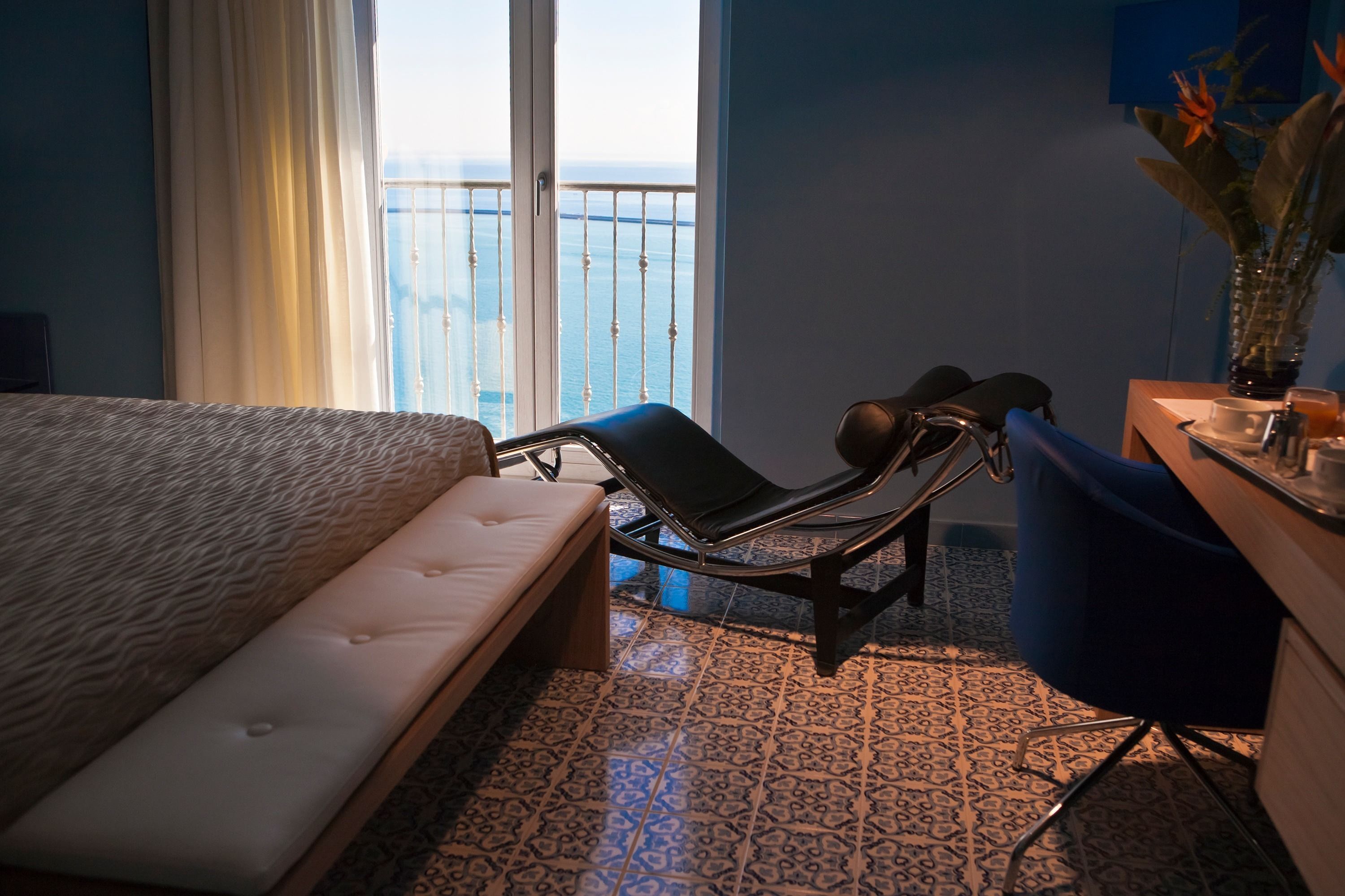 Camera d'hotel con un letto, una sedia, una scrivania e vista mare da un balcone.