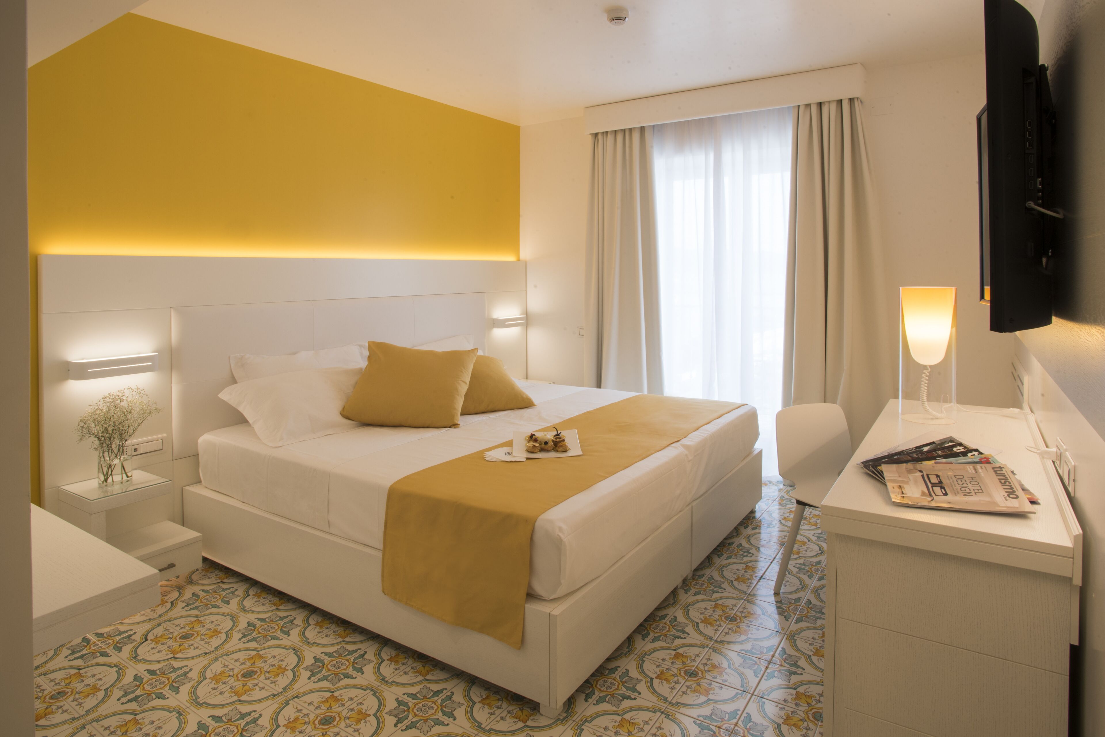 A hotel room with a large bed, bedside tables, a desk with a lamp, and a TV.