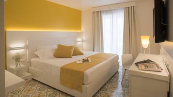 A hotel room with a large bed, bedside tables, a desk with a lamp, and a TV.