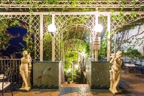 Una escalera de losa con barandilla de metal, rodeada de follaje y una estructura de celosía blanca.