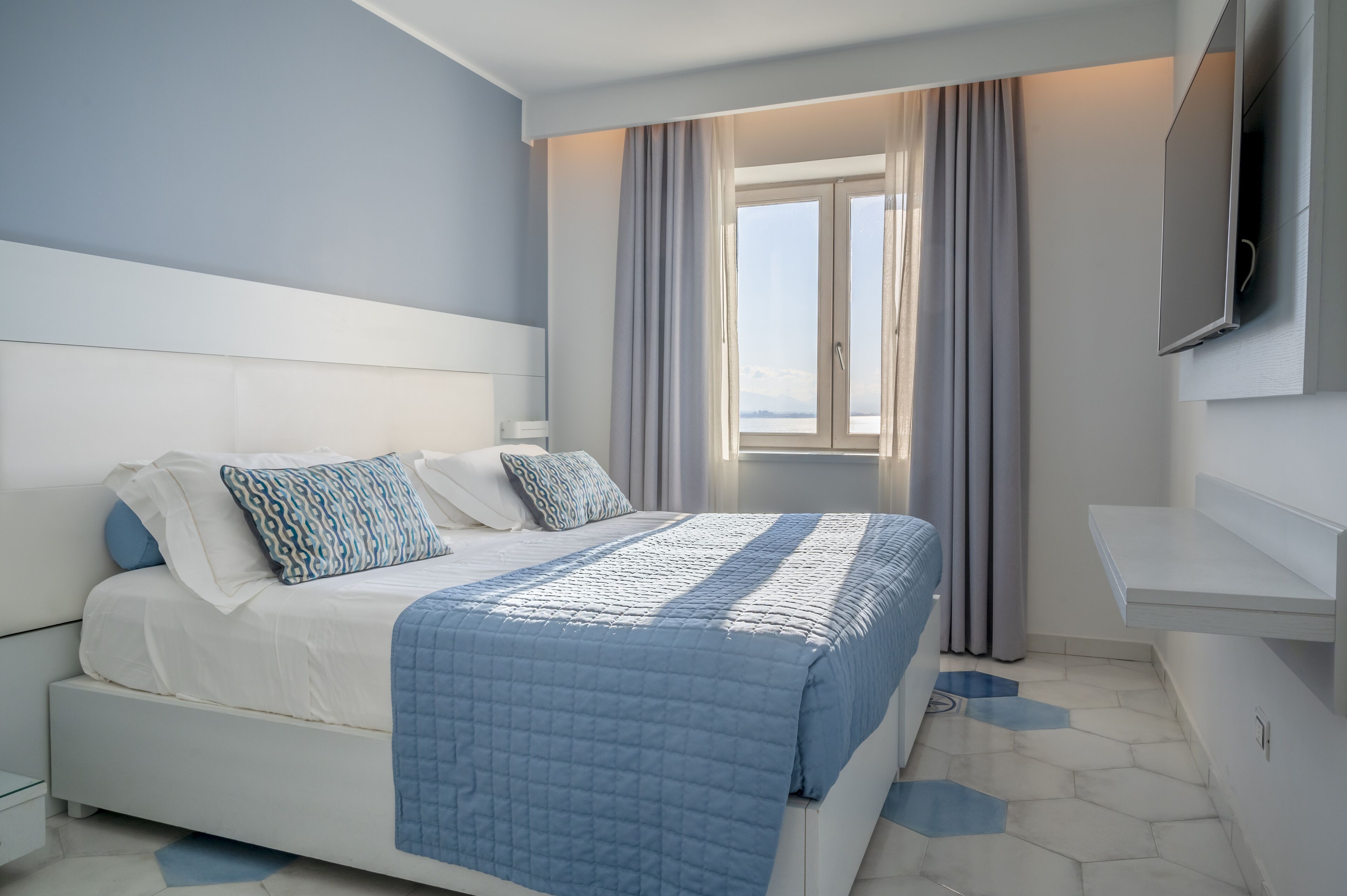 A modern hotel room with a large bed, a TV mounted on the wall, and a window with curtains.