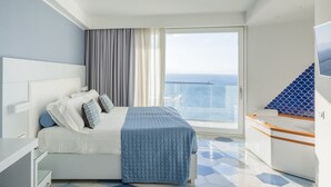 Habitación de hotel moderna con una cama grande, vistas al mar, un balcón y un baño pequeño.