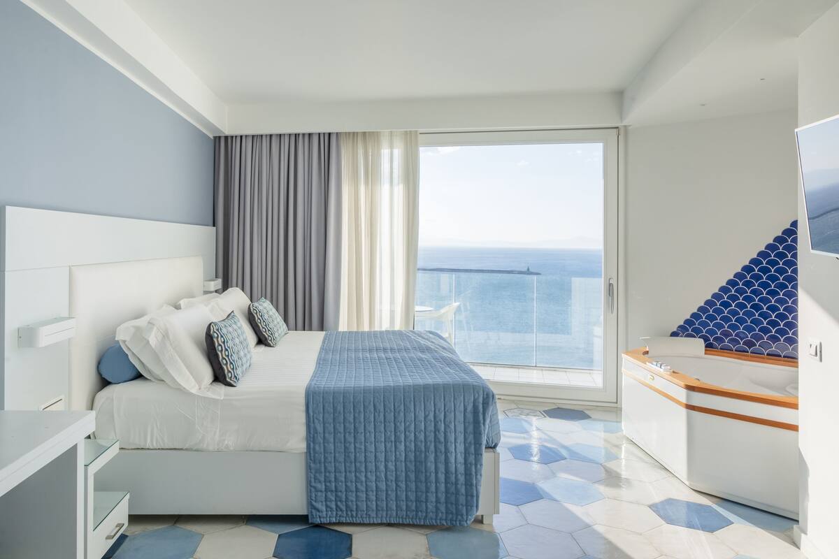 Habitació d'hotel moderna amb un llit gran, vista al mar, un balcó i un bany petit.