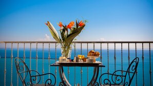 Un balcón con una mesa preparada para el desayuno, con vista a un mar azul y despejado.