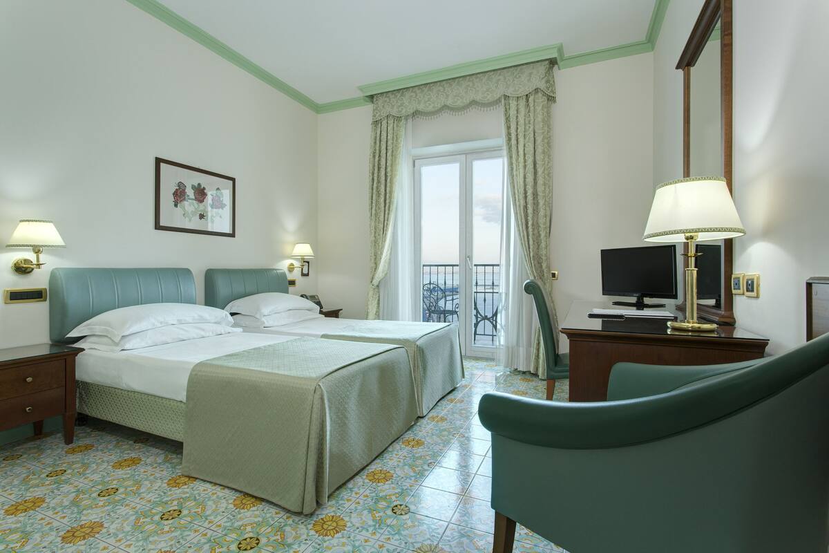 Habitació d'hotel amb dos llits, un escriptori amb televisió, una cadira i un balcó amb vistes.