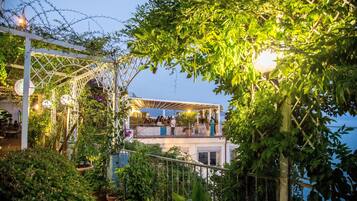 Una terraza exterior con una pérgola blanca, plantas en macetas y un área de piscina.