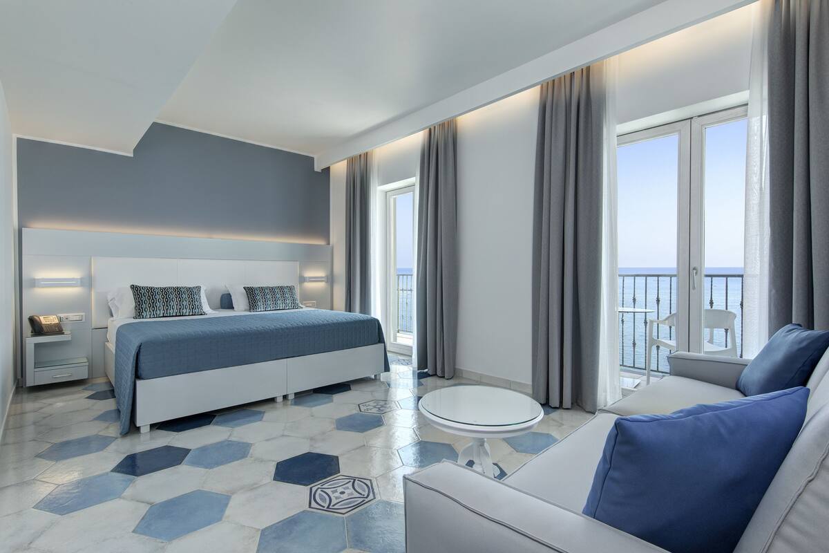 Habitació d'hotel moderna amb un llit, un sofà, una taula rodona i un balcó amb vistes.