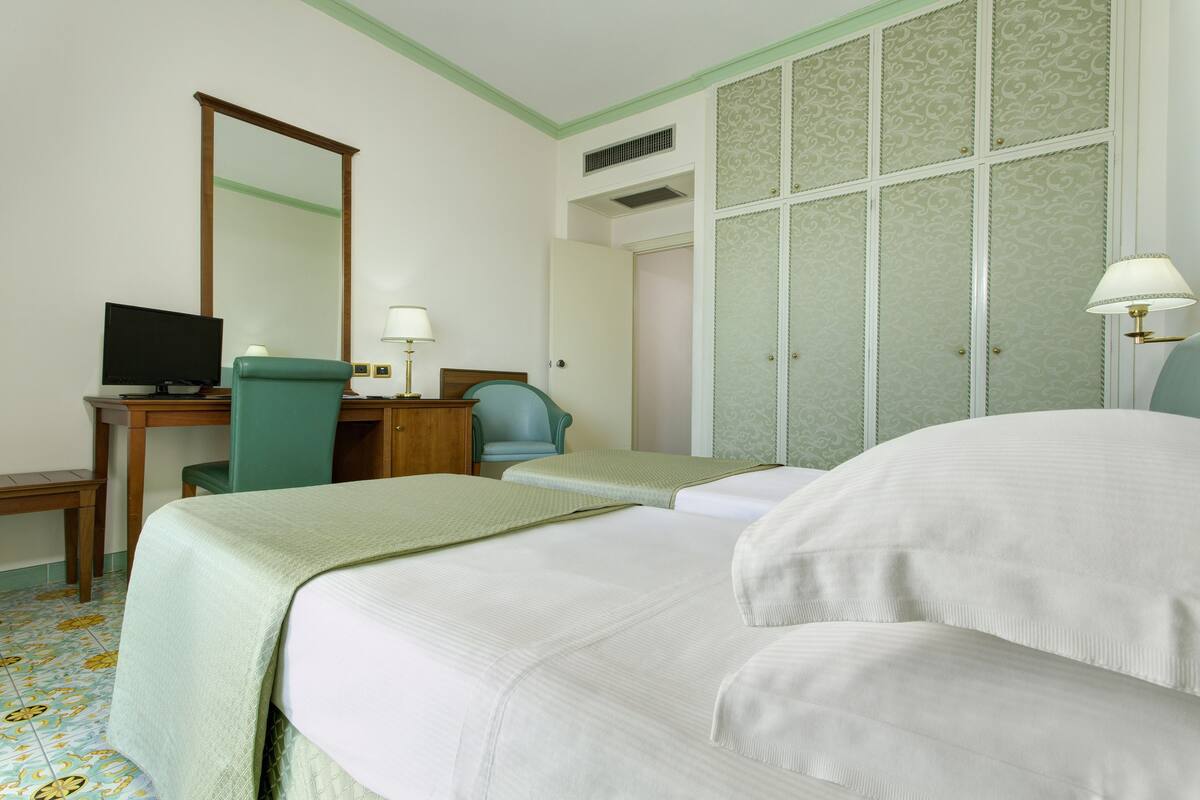 Habitació d'hotel amb dos llits, un escriptori amb un ordinador, una cadira, un mirall i un armari.