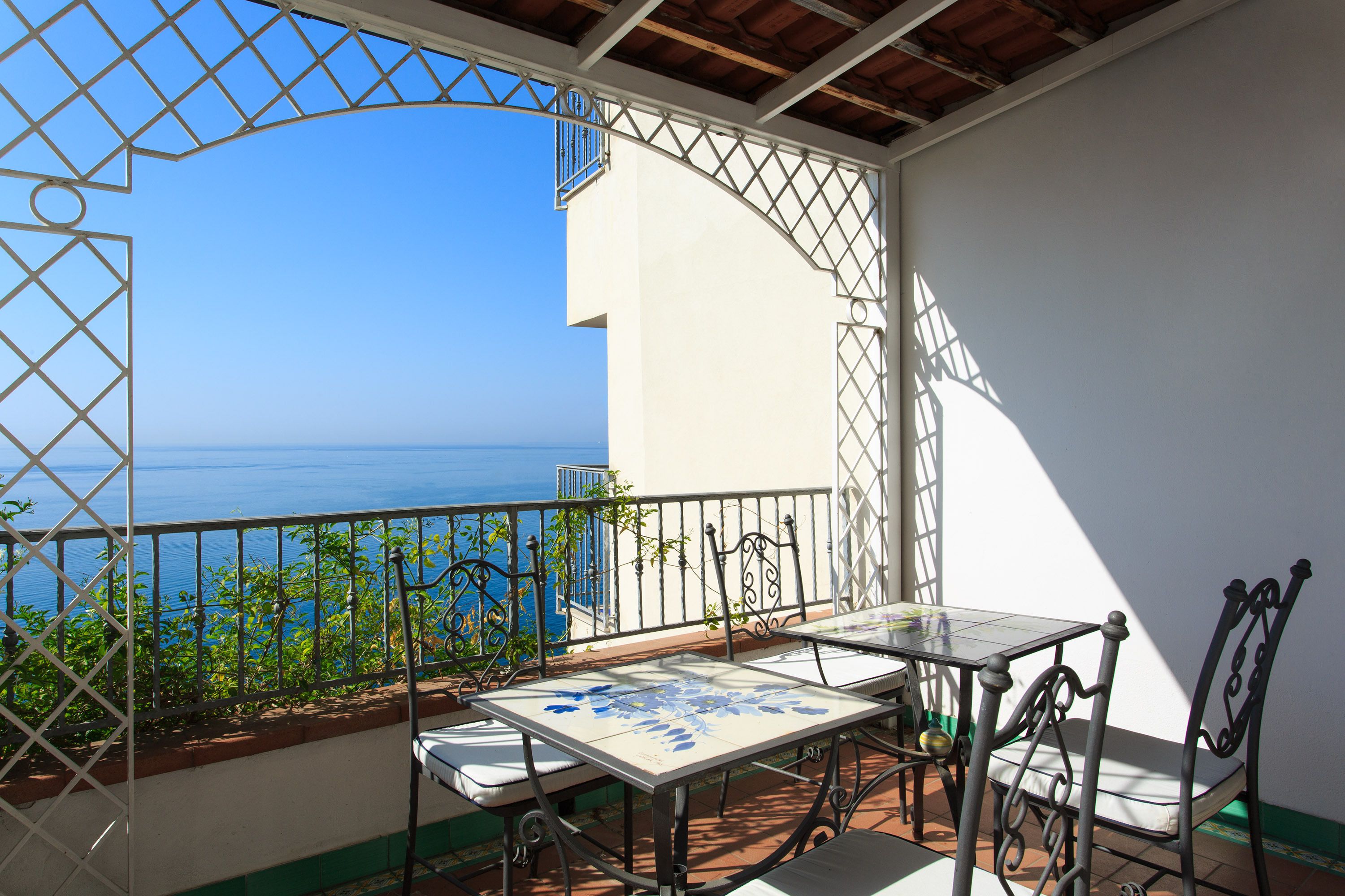 A balcony with a table and chairs, overlooking a clear blue sea.