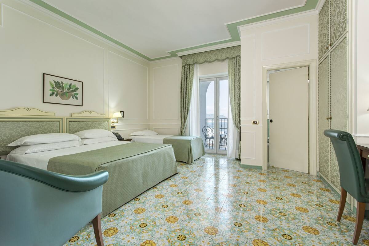 Habitació d'hotel amb llit, una cadira, escriptori i un balcó amb vistes.