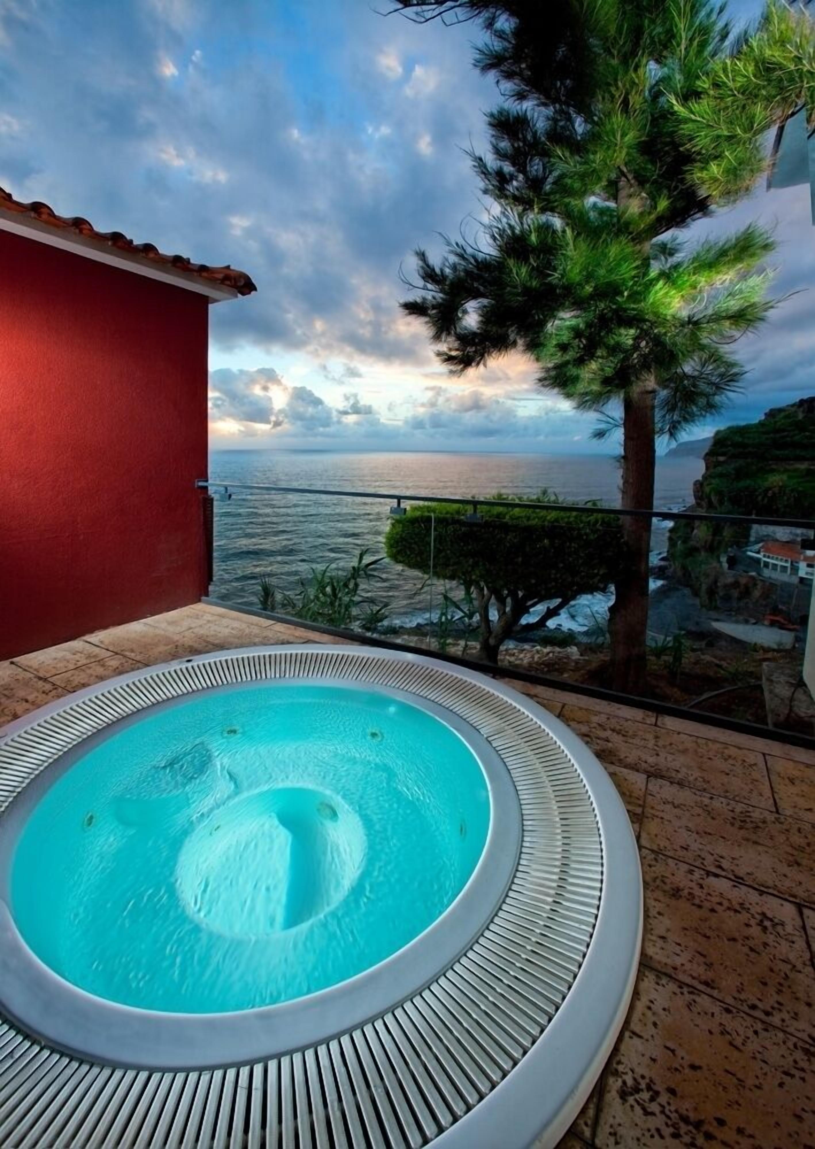 Un bain à remous avec vue sur l’océan et un bâtiment rouge en arrière-plan.