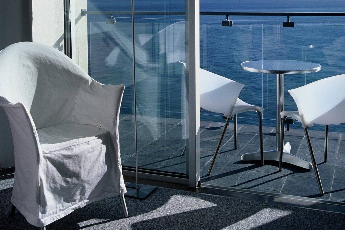 Un balcon avec une table et des chaises en verre, une lampe sur pied et une vue sur l’océan.