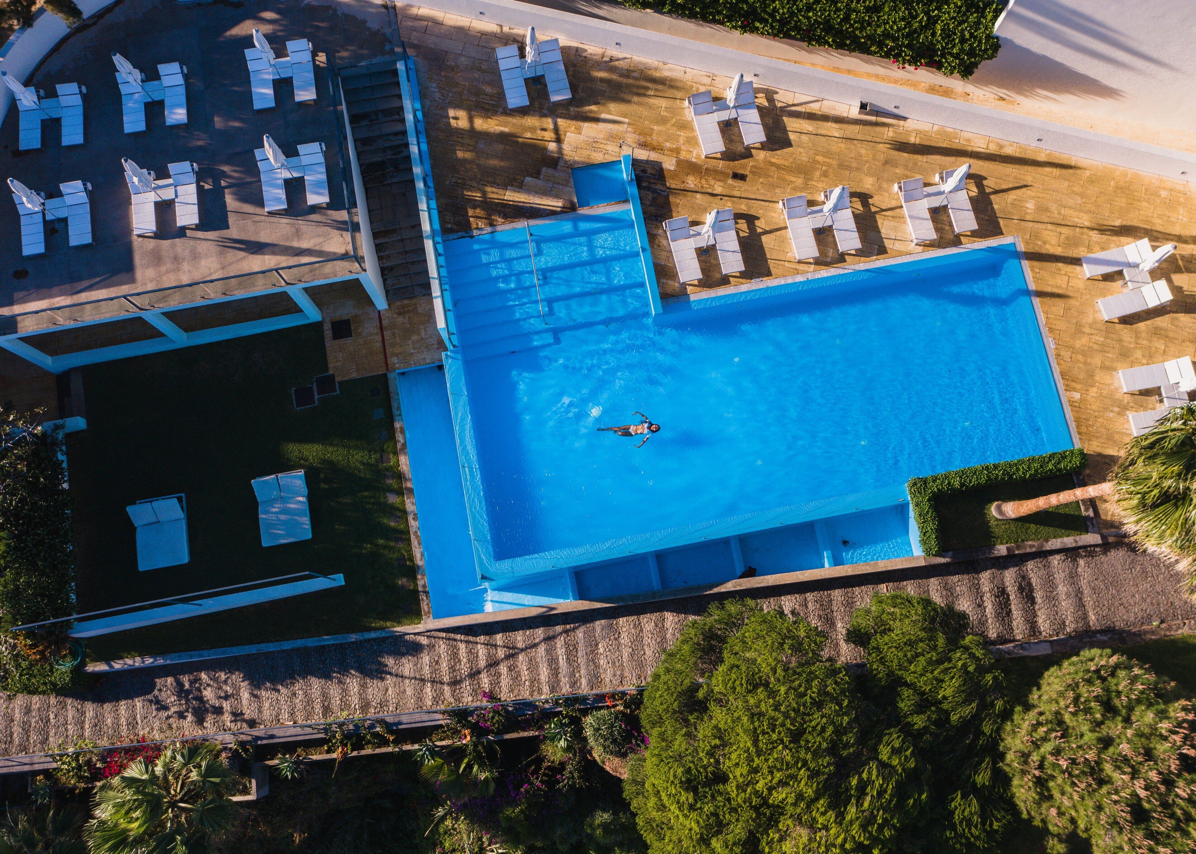 Vue aérienne d’un hôtel doté d’une grande piscine, de chaises longues et d’un espace abrité avec des parasols.