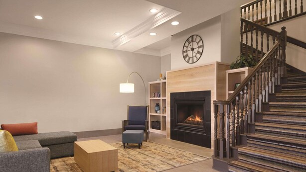 A living room with a fireplace, a staircase, and a clock on the wall. - Country Inn & Suites by Radisson, Billings, MT (Billings)
