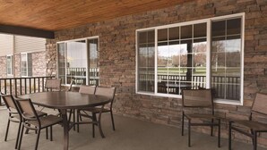 An outdoor patio with a round table and chairs, stone walls, and large windows. - Country Inn & Suites by Radisson, Billings, MT (Billings)