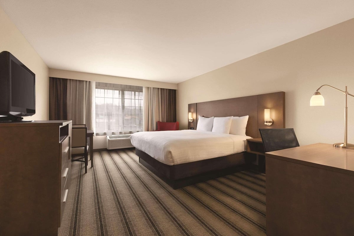 A hotel room with a large bed, a desk, a television, and a window with curtains.