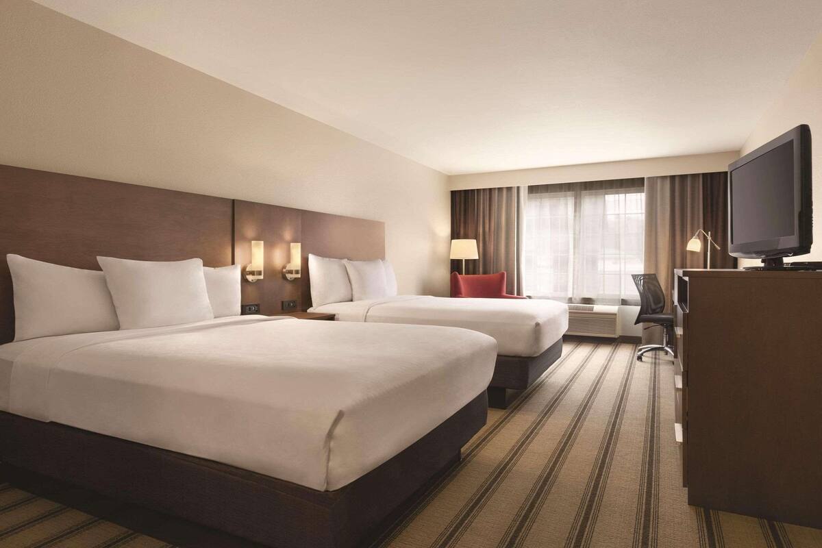A hotel room with two beds, a desk, a television, and a window with curtains.