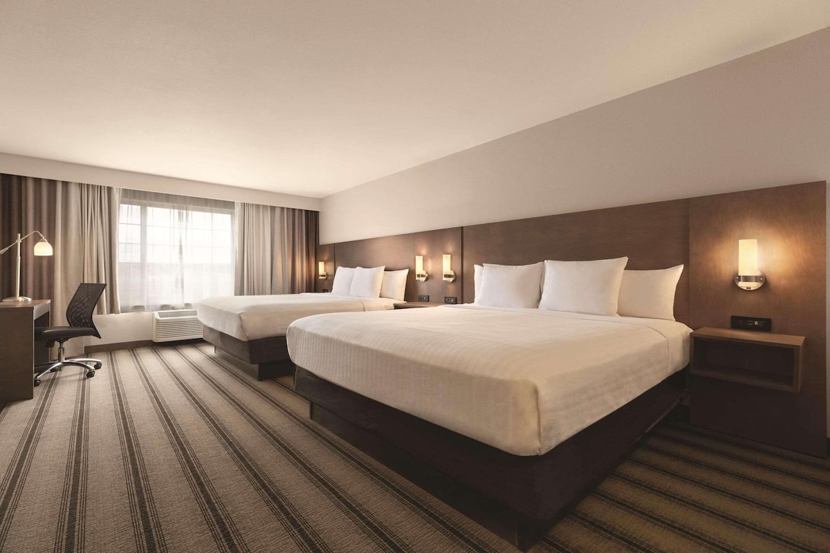 A hotel room with two beds, a desk, and a chair.