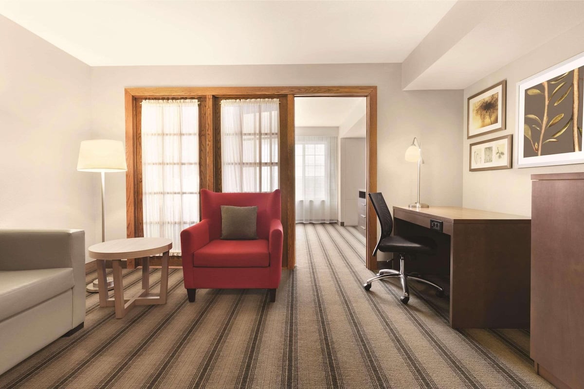 A hotel room with a red armchair, a white sofa, a small round table, a desk with a chair, and a large mirror.