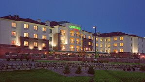 A multi-story hotel with a prominent 'Courtyard' sign, featuring a brick facade, multiple balconies, and a well-lit entrance area. - Courtyard by Marriott Madison East (Madison)
