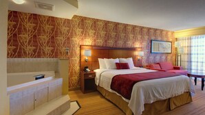 A hotel room with a large bed, a sitting area with a red sofa, a small table, and a bathtub. - Courtyard by Marriott Madison East (Madison)