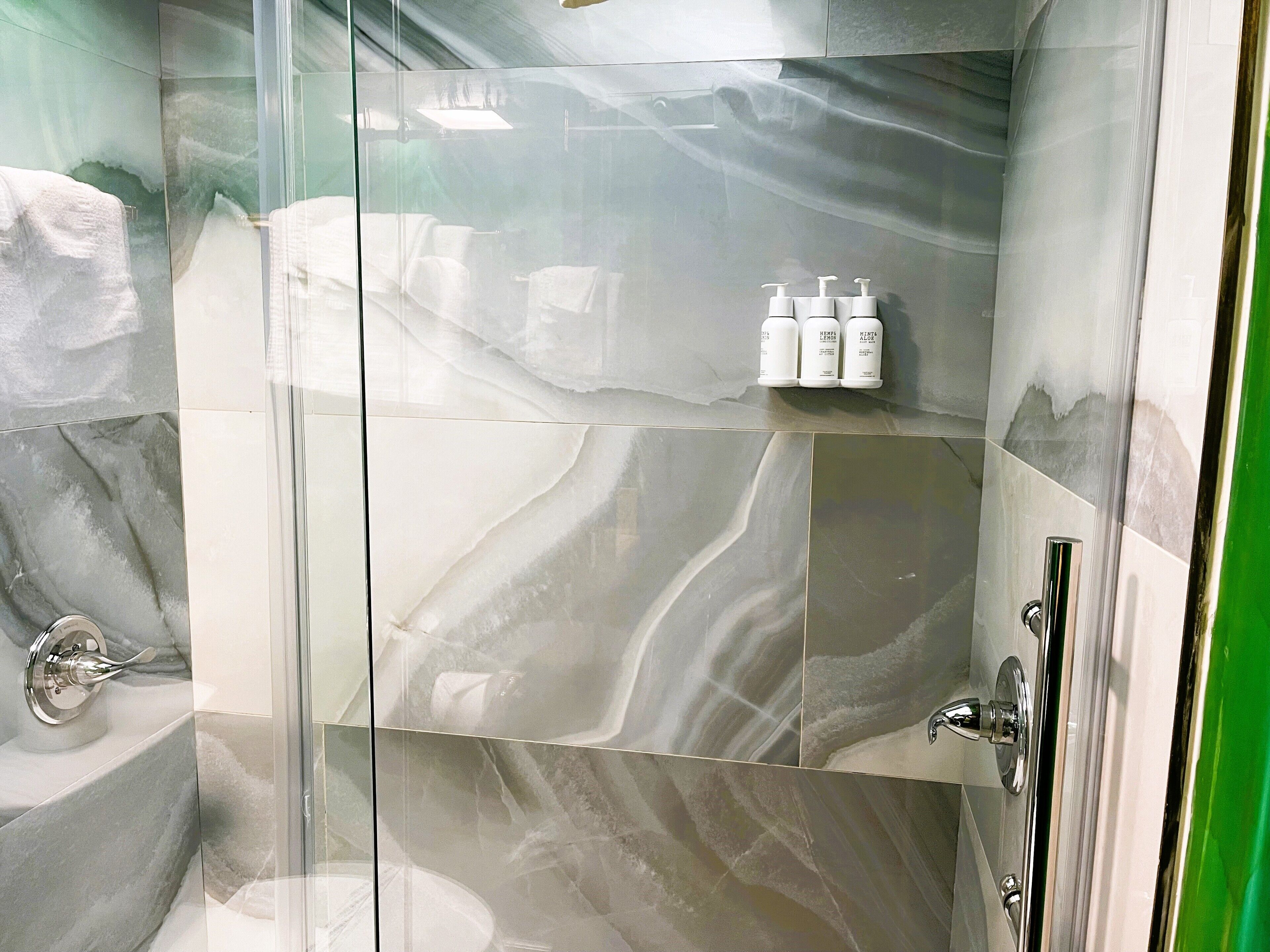Un baño moderno con cabina de ducha de vidrio, azulejos de mármol y un estante con artículos de aseo.