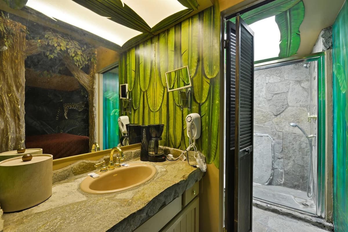 Un baño con lavamanos de piedra, un espejo, un secador de pelo y una ducha con pared de piedra.