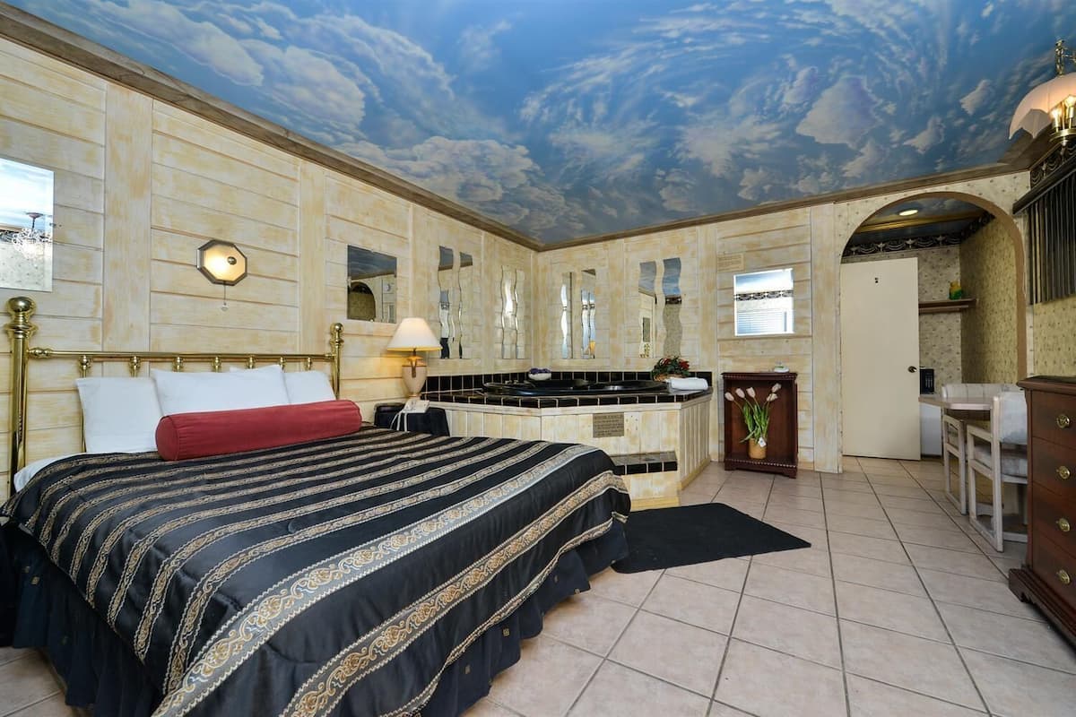 Habitación de hotel con una cama grande, un escritorio, una tocador y un mural en el techo.