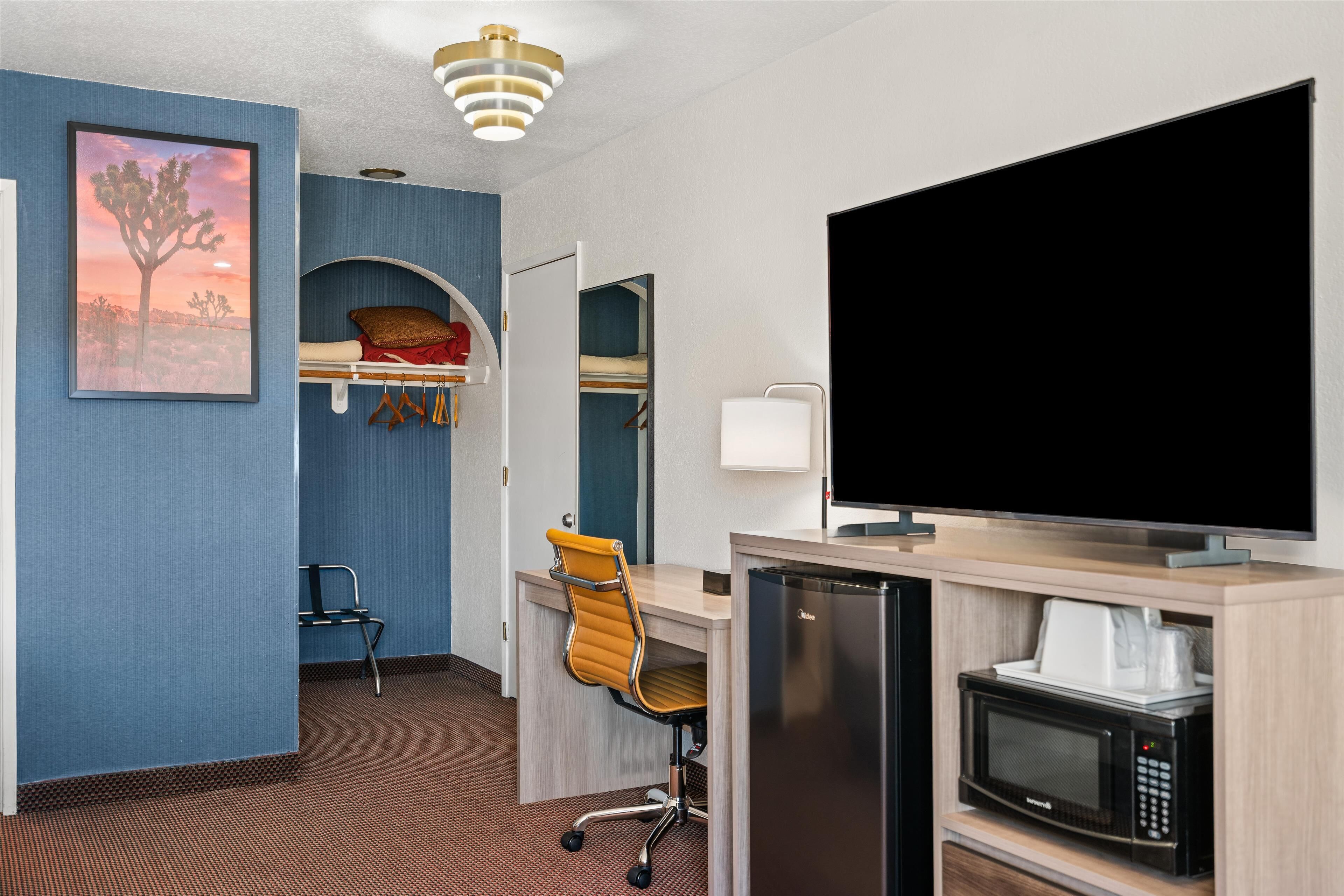 Une chambre d’hôtel équipée d’un lit, d’un bureau avec un ordinateur, d’un four à micro-ondes, d’une télévision et d’une chaise.