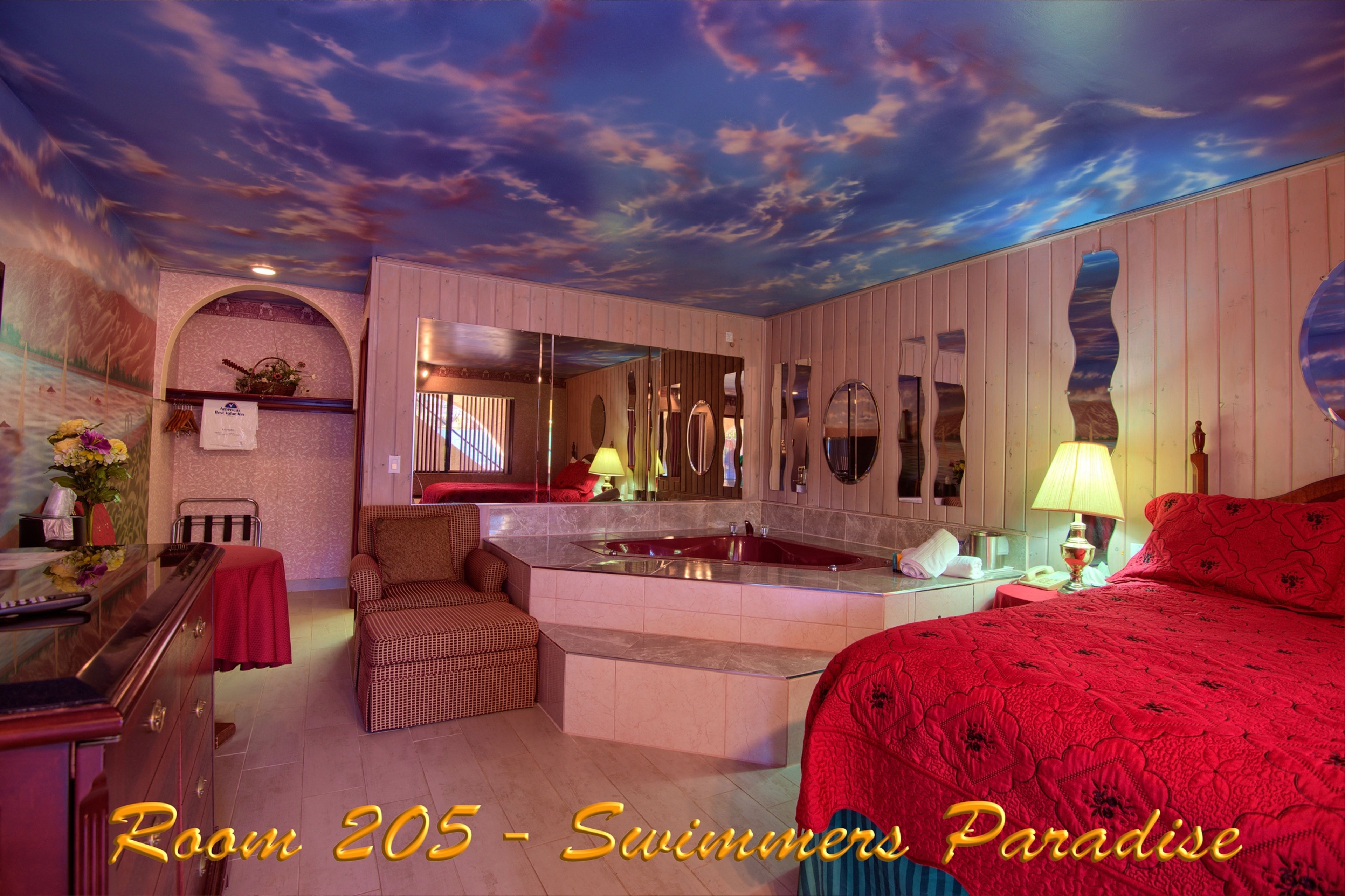 A room with a large bed, a sitting area, a bathtub, and a mirror.