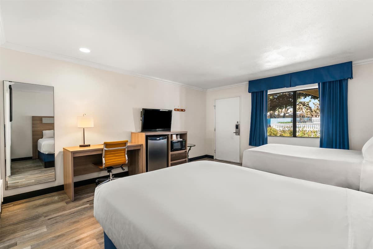 Habitación de hotel con cama, escritorio, silla, televisor y vistas al exterior.