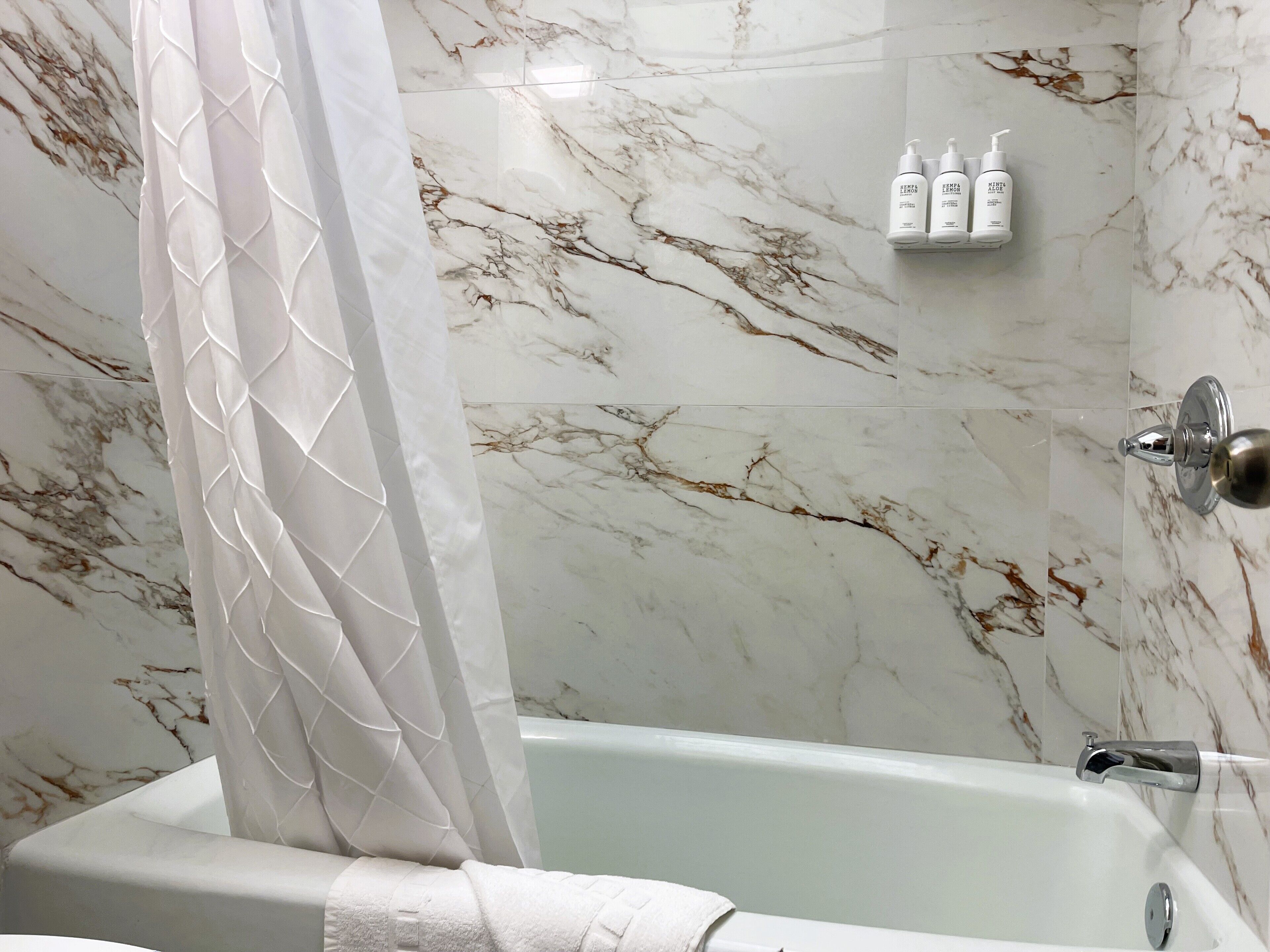 Un bagno con una vasca, pareti in marmo, un telo da doccia e articoli da toilette su uno scaffale.