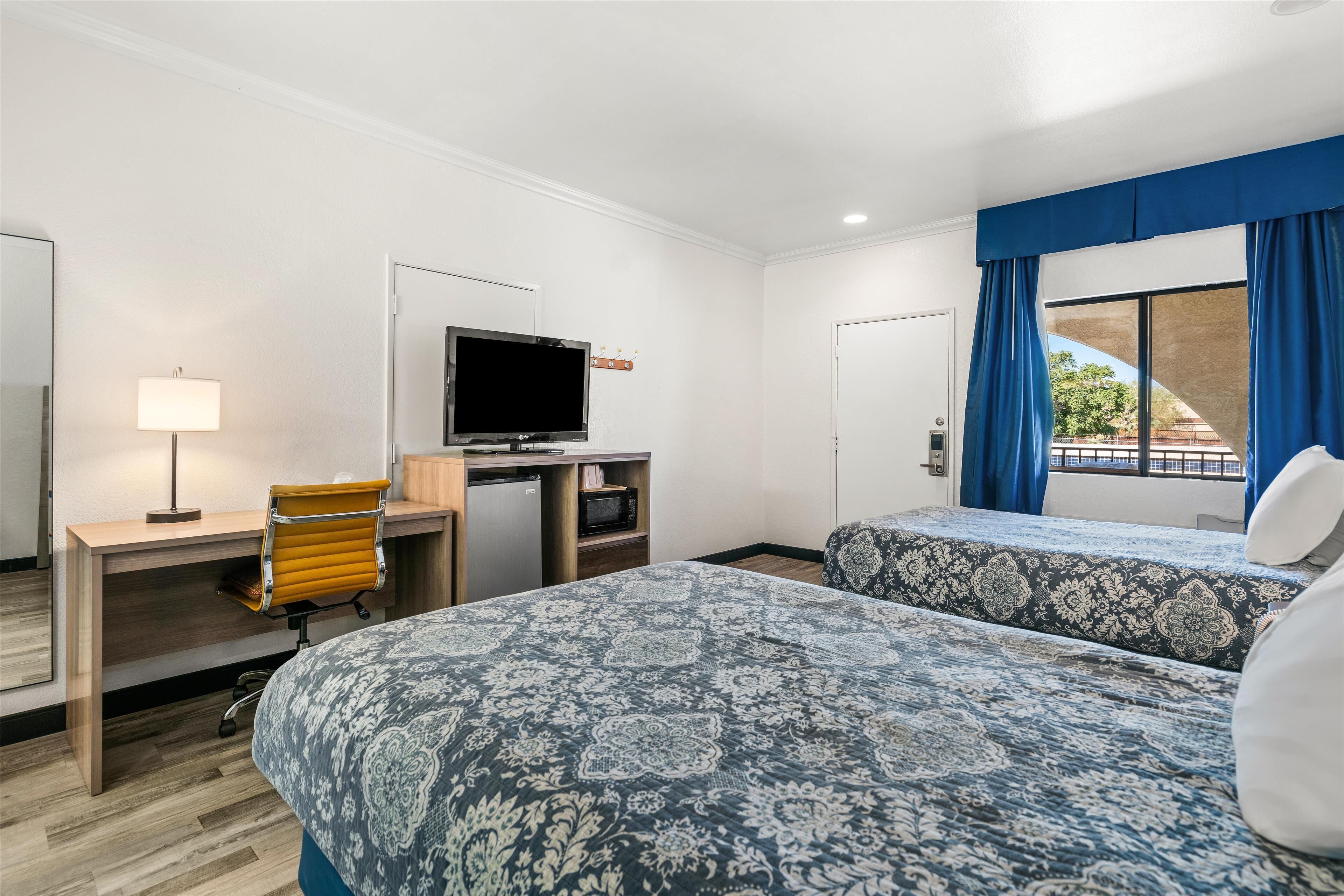 A hotel room with two beds, a desk with a computer, a TV, and a window with curtains.