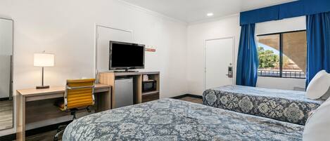 A hotel room with two beds, a desk with a computer, a TV, and a window with curtains.