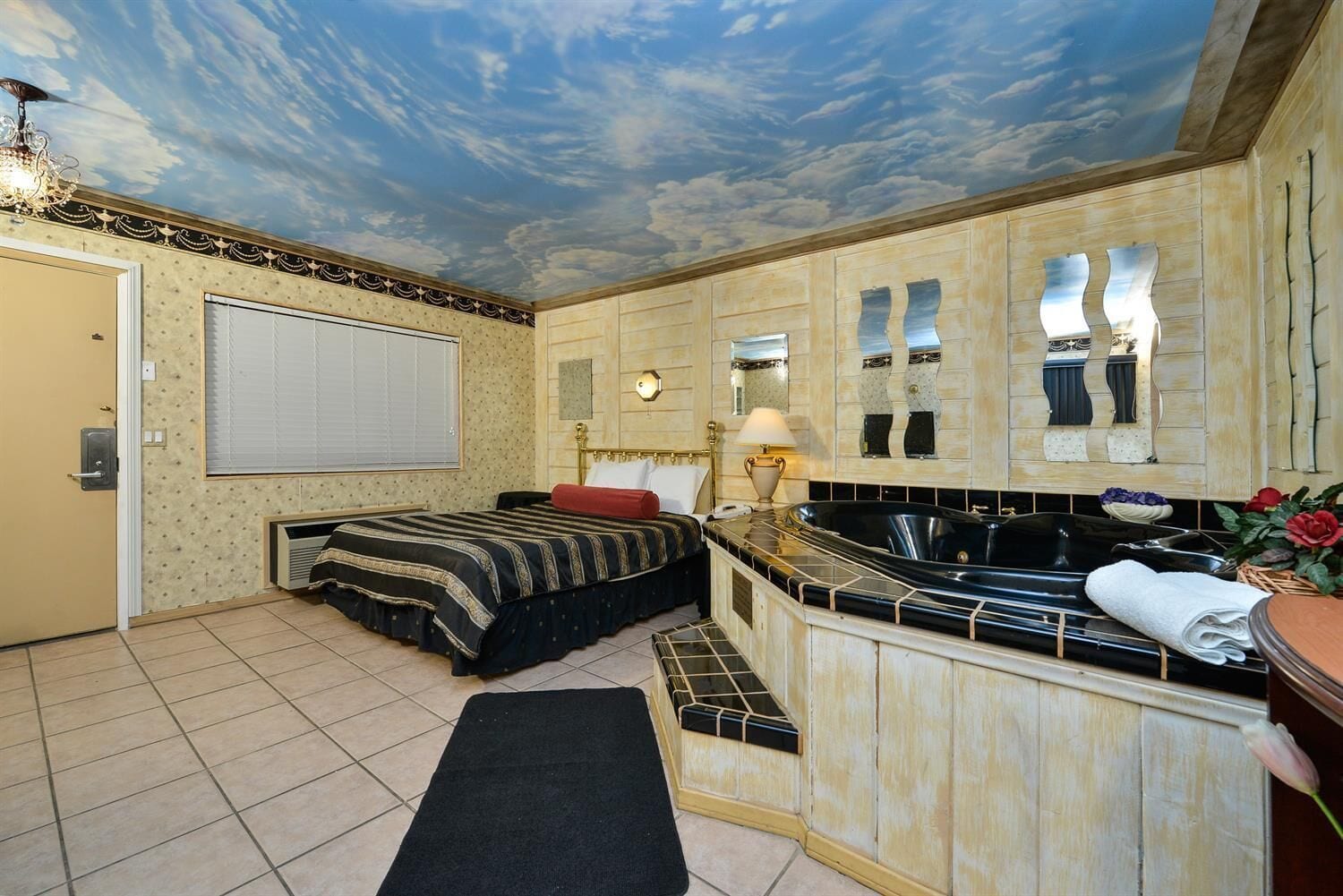 A room with a bed, a bathtub, a sink, and a mirror.