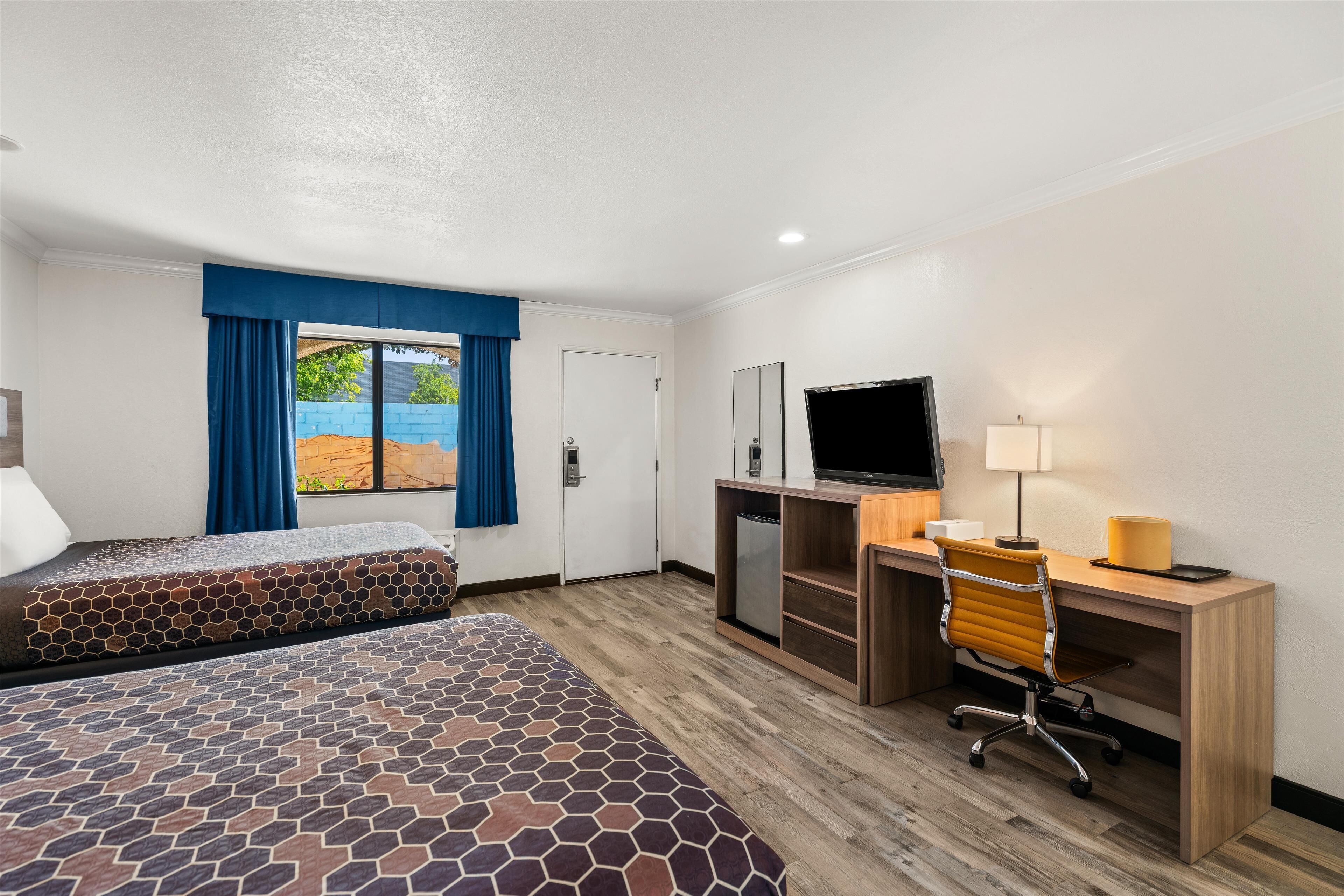 A hotel room with two beds, a desk with a computer, a TV, and a window with curtains.