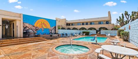 Un área de piscina en la azotea con dos jacuzzis, sillones de descanso y un mural en la pared.