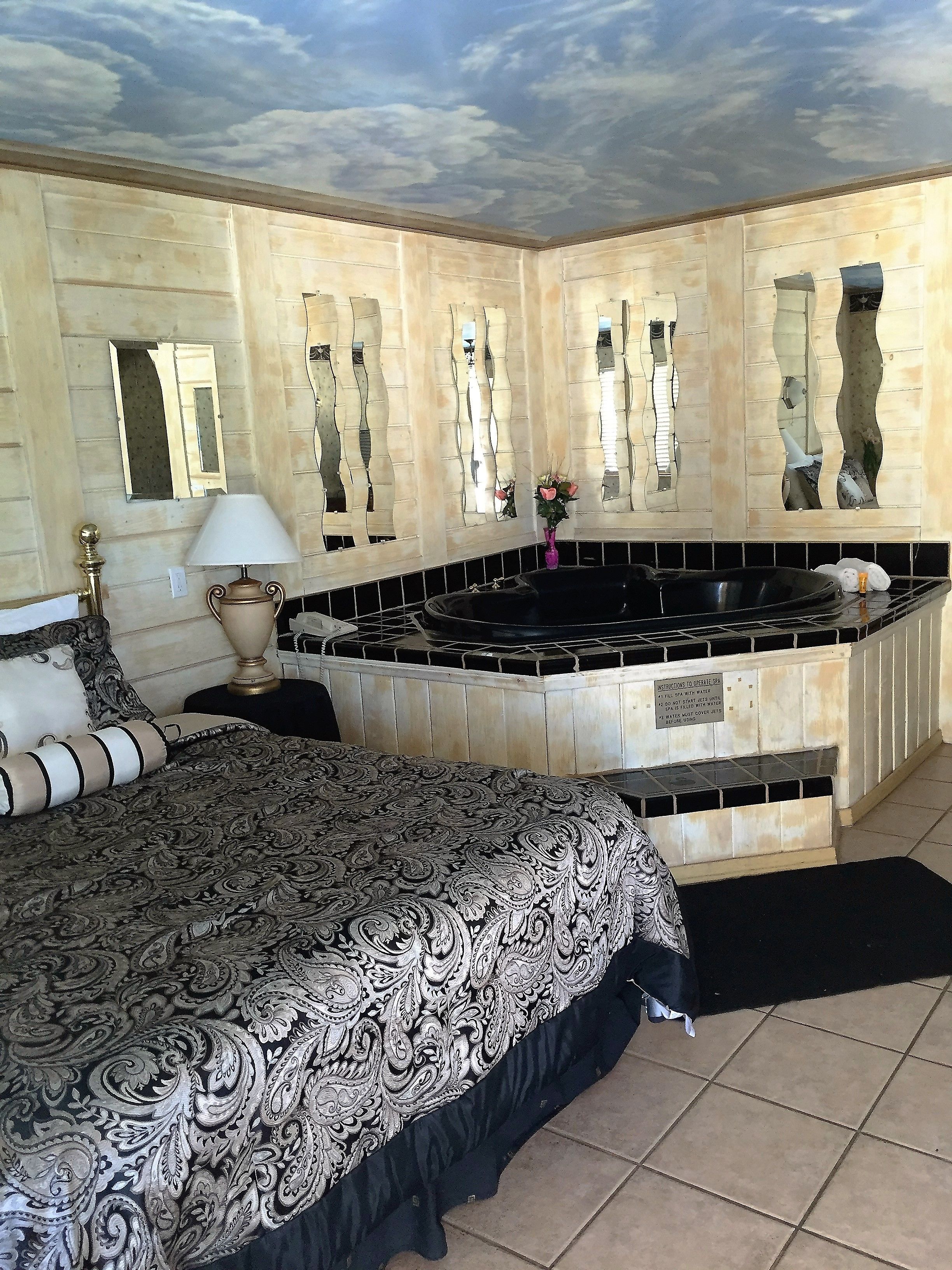 A hotel room with a large bed, a bathtub, and a ceiling mural.
