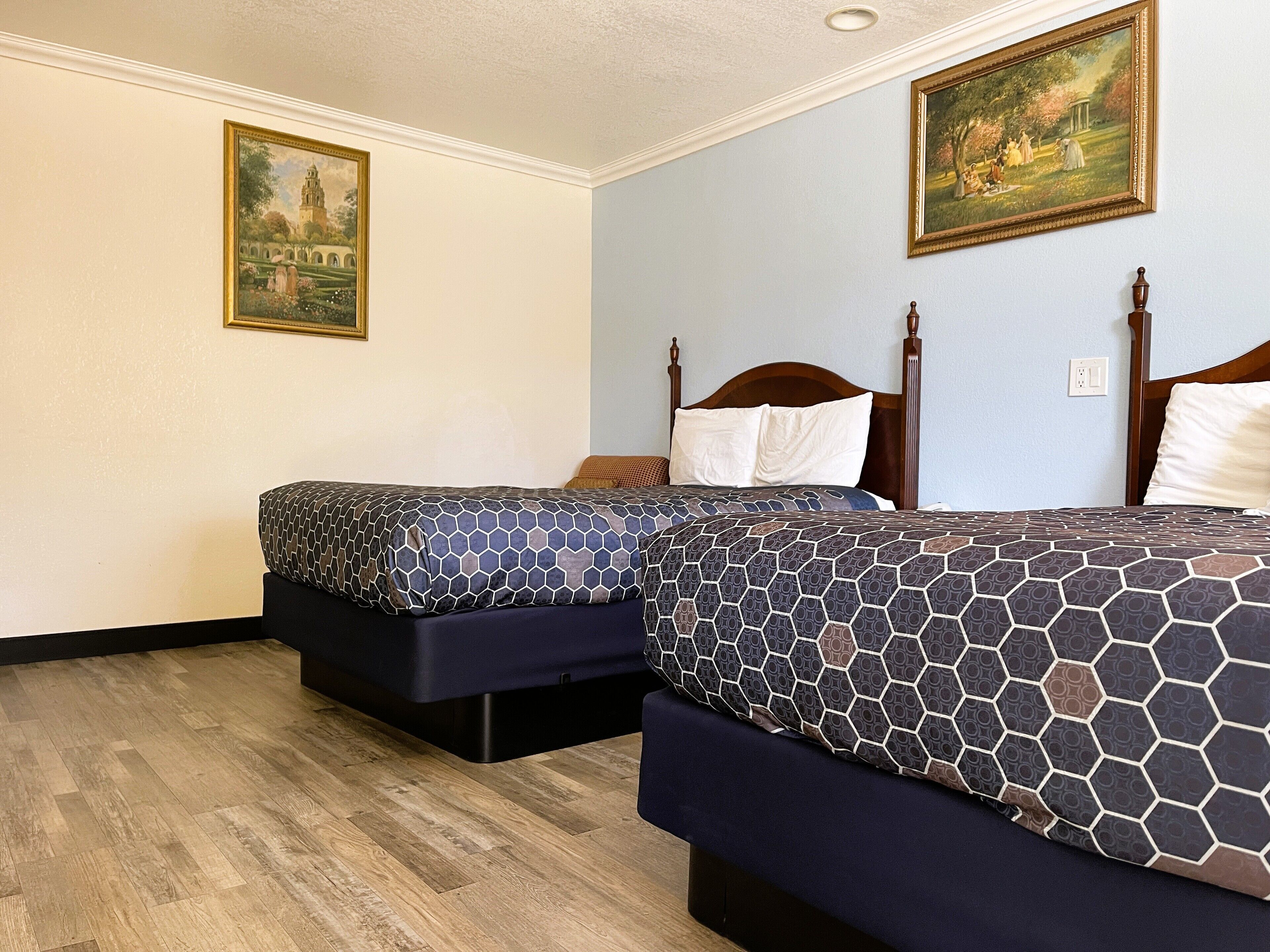 A hotel room with two beds, wooden headboards, and a painting on the wall.