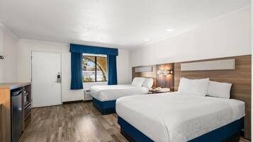A hotel room with two beds, a desk, and a window with blue curtains.