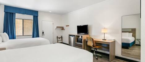 A hotel room with two beds, a desk with a chair, a television, a mirror, and a window with curtains.