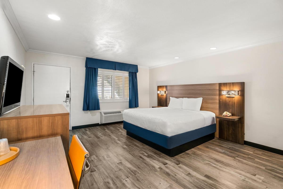 Una habitación de hotel con una cama, un escritorio, un televisor y una mesita de noche.