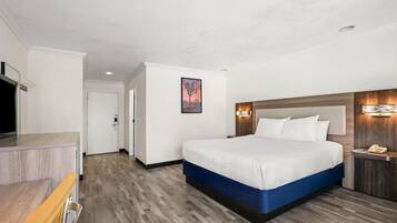 A hotel room with a large bed, a wooden headboard, a bedside table with a lamp, and a flat-screen TV.