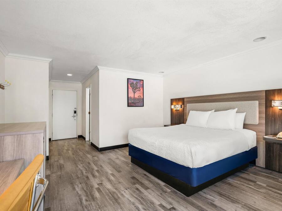 A hotel room with a large bed, a wooden headboard, a bedside table with a lamp, and a flat-screen TV.