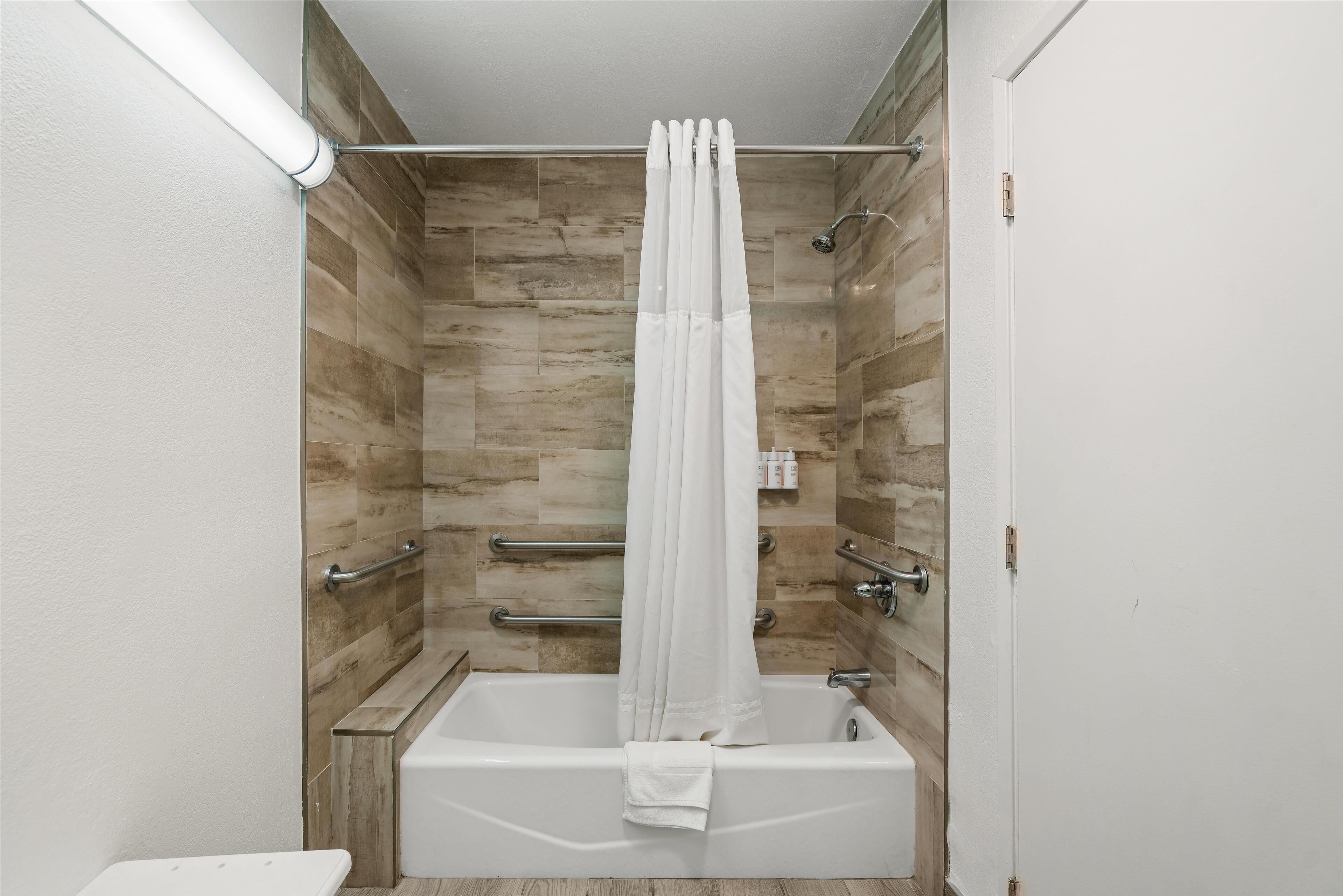A modern bathroom with a bathtub, a shower curtain, and a handrail.